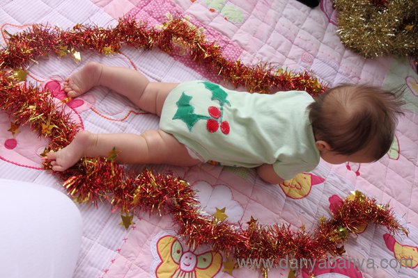 Holly on the bottom of baby Bee's onesie with tinsel