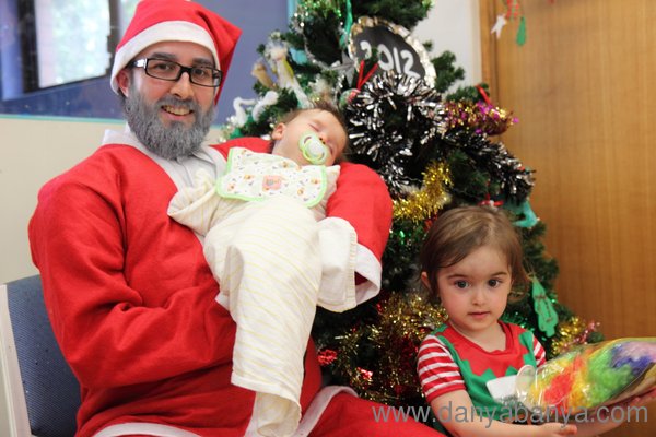 Mr Banya dressed as Santa, holding baby Bee with JJ standing